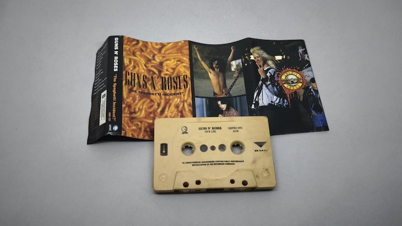May include: A Guns N' Roses cassette tape and album art. The cassette is beige with text and holes. The album art features a spaghetti image and band members. The album is titled "The Spaghetti Incident?"