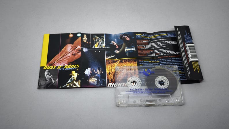 May include: A clear cassette tape with a black and white label, and a folded album cover. The album cover features images of a band performing on stage, with the text "Dust N' Bones It's Alright" and "NIGHTRAIN".
