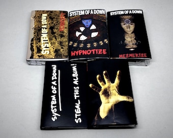 May include: Five System of a Down cassette tapes arranged in two rows. The top row features the self-titled album, Hypnotize, and Mezmerize. The bottom row includes Steal This Album! and a cassette with a hand graphic. Each tape displays band and album text.