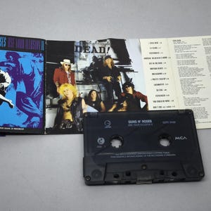 May include: A Guns N' Roses cassette tape with the album cover art for "Use Your Illusion II" and a tracklist insert. The cassette is black, and the album art features a blue and purple design. The album cover is open, displaying band members.