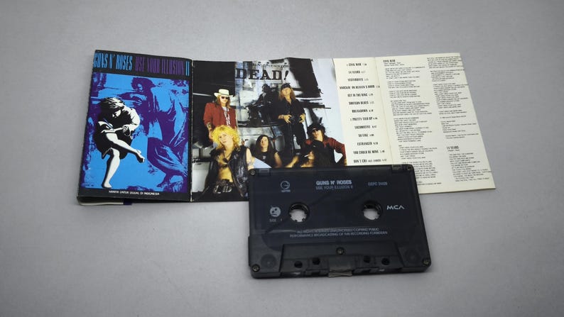 May include: A Guns N' Roses cassette tape with the album cover art for "Use Your Illusion II" and a tracklist insert. The cassette is black, and the album art features a blue and purple design. The album cover is open, displaying band members.
