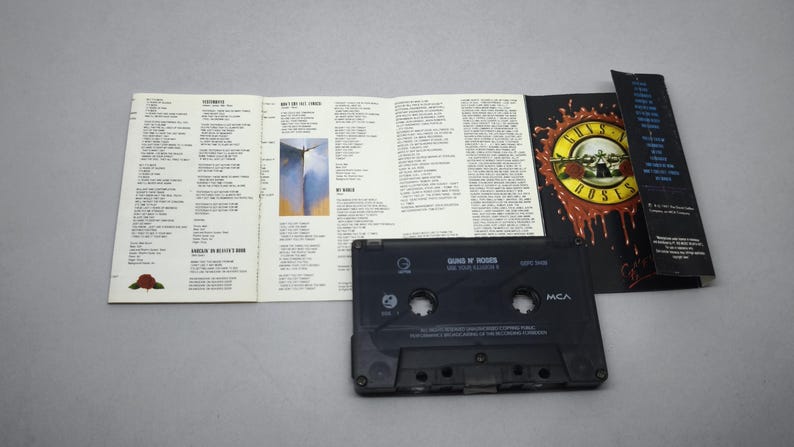 May include: A black cassette tape and the accompanying booklet for Guns N' Roses' album, "G N' R Lies." The album art features a skull with roses and the band's name. The booklet is open, displaying song lyrics.
