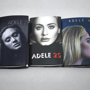 May include: Three music albums featuring Adele. The left cover shows Adele in black and white with the text ADELE 21. The center cover features a portrait of Adele with the text ADELE 25. The right cover shows a profile of Adele with the text ADELE 30.