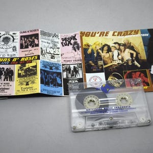 May include: A Guns N' Roses cassette tape with a multi-panel album insert. The insert features concert posters and band photos. The cassette is clear with a blue label. The album cover reads "You're Crazy".
