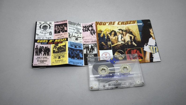 May include: A Guns N' Roses cassette tape with a multi-panel album insert. The insert features concert posters and band photos. The cassette is clear with a blue label. The album cover reads "You're Crazy".