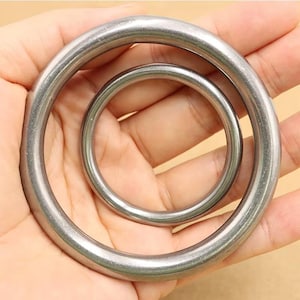 May include: Two circular metal rings with a smooth, polished silver-toned finish. The rings are nested, with one smaller ring positioned inside the center of a larger ring. Both rings feature a consistent, rounded cross-section and metallic texture.