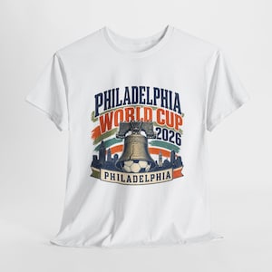 May include: White t-shirt featuring a graphic design for the Philadelphia World Cup 2026. The design includes the words "Philadelphia World Cup 2026" with a Liberty Bell, soccer ball, and city skyline.