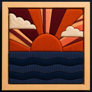 May include: A square fabric wall art piece in a light wood frame featuring a sunset scene. The design includes a semi-circular orange sun, radiating beams of burgundy and orange fabric, and two cream-colored clouds above dark blue wavy ocean waves.