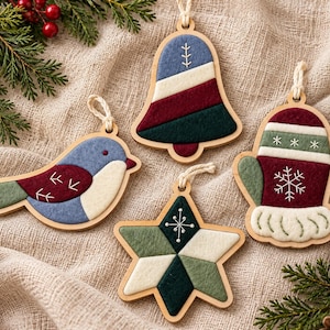 May include: Four wooden holiday ornaments featuring felt inlays in shades of blue, red, green, and cream. The shapes include a bird, a bell, a star, and a mitten, each with white embroidered details and a small loop for hanging on a string.