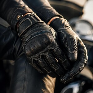 Könnte beinhalten: Schwarze Motorradhandschuhe aus Leder mit perforierten Einsätzen, verstärktem Knöchelschutz und hellen Kontrastnähten. Die Handschuhe verfügen über gepolsterte Fingerbereiche und einen sicheren Handgelenkverschluss mit einem Metallknopf.