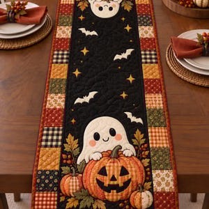 May include: A rectangular quilted table runner featuring a black center panel with two white ghosts, orange jack-o'-lantern pumpkins, autumn leaves, and white bats. The border consists of a patchwork pattern of squares in orange, green, and black.