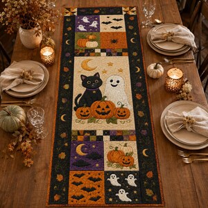 Könnte beinhalten: Ein rechteckiger, gesteppter Tischläufer mit Halloween-Motiven, darunter Applikationen von einer schwarzen Katze, einem weißen Geist, orangefarbenen Kürbissen, Fledermäusen und Mondsicheln auf einem cremefarbenen Mittelteil.