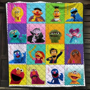 May include: A quilted blanket featuring a grid of sixteen Sesame Street characters including Big Bird, Ernie, Bert, Cookie Monster, Rosita, The Count, Oscar the Grouch, Abby Cadabby, Herry Monster, Julia, Guy Smiley, Mr. Snuffleupagus, Elmo, Telly, Grover, and Zoe.