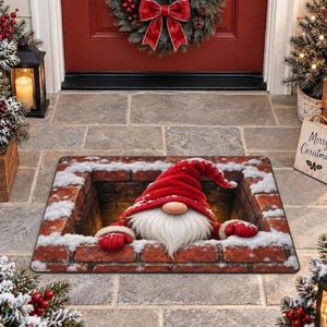 Puede incluir: Un felpudo rectangular con una ilustración en 3D de un gnomo con barba blanca larga y gorro rojo que emerge de una chimenea de ladrillo cubierta de nieve. El gnomo lleva manoplas rojas y parece estar saliendo de la chimenea.