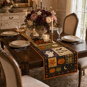 May include: A rectangular fabric table runner featuring a patchwork design with Halloween motifs including pumpkins, a white ghost, black bats, autumn leaves, and crescent moons in orange, black, purple, and green colors on a dark background.