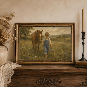 May include: A framed vintage painting depicts a child in denim overalls walking with a horse through a field of wildflowers. The painting has a gold ornate frame. The scene is set on a wooden surface with candles and a vase of dried flowers.