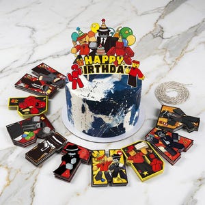 May include: A birthday cake with blue and white icing, decorated with cartoon characters and a "Happy Birthday" cake topper. The cake is surrounded by matching decorative cards and a length of string.