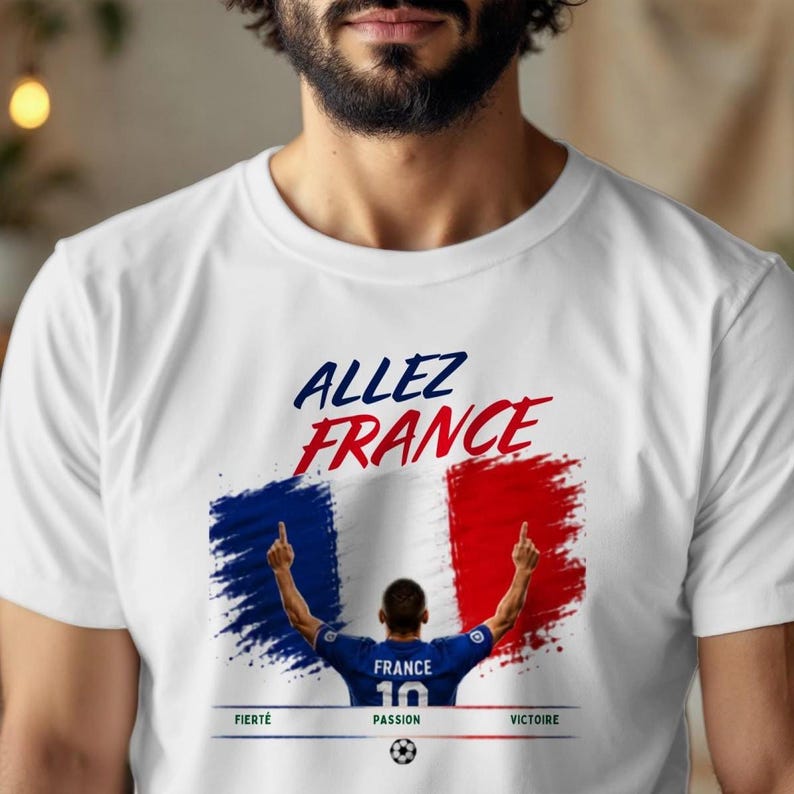 May include: A white t-shirt featuring a graphic of a soccer player in a blue jersey with the number 10, set against a French flag background. The text reads "ALLEZ FRANCE" at the top and "FIERT&Eacute;", "PASSION", "VICTOIRE" at the bottom with a soccer ball.