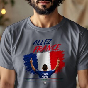 May include: A charcoal gray t-shirt featuring a graphic of a soccer player in a blue jersey with the number 10, standing before a French flag design. The text reads "ALLEZ FRANCE" in blue and red, with "FIERT&Eacute;", "PASSION", and "GLOIRE" below.