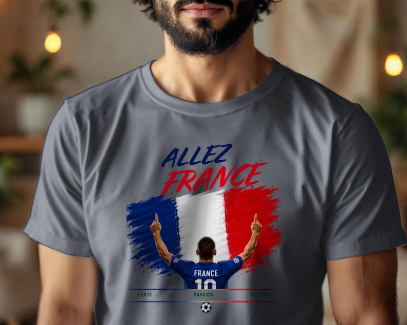 May include: A charcoal gray t-shirt featuring a graphic of a soccer player in a blue jersey with the number 10, standing before a French flag design. The text reads "ALLEZ FRANCE" in blue and red, with "FIERT&Eacute;", "PASSION", and "GLOIRE" below.