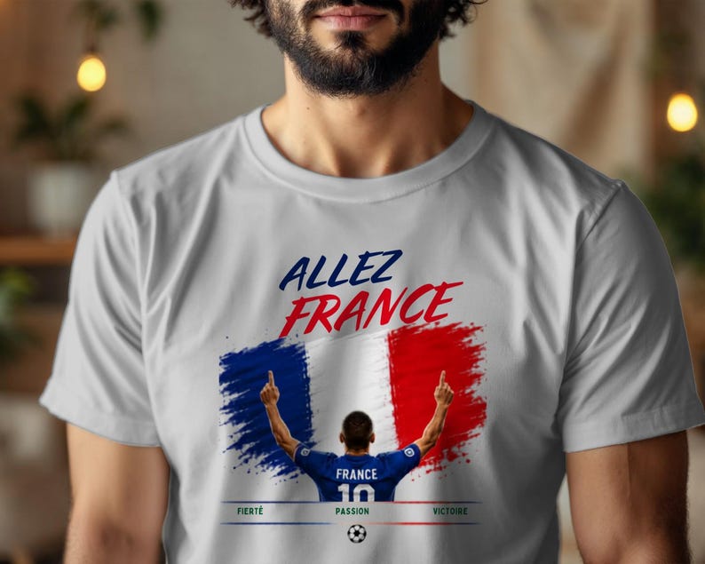 May include: A light gray t-shirt featuring a graphic of the French flag in a brushstroke style. Above the flag, the text reads ALLEZ FRANCE. Below, a soccer player in a blue jersey with the number 10 is shown, with the words FIERT&Eacute;, PASSION, VICTOIRE.