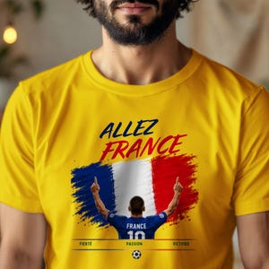May include: A bright yellow short-sleeved t-shirt featuring the text ALLEZ FRANCE in dark blue and red. Below, a graphic shows a soccer player in a blue jersey with the number 10, set against a French flag background, with FIERT&Eacute;, PASSION, VICTOIRE.