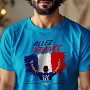 May include: A bright blue t-shirt featuring the text "ALLEZ FRANCE" in dark blue and red. Below, a graphic shows a soccer player in a blue jersey with "FRANCE 10" on the back, standing before a French flag. The words "FIERT&Eacute;", "PASSION", and "VICTOIRE" appear below.