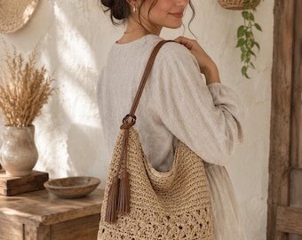 May include: A beige woven straw hobo bag featuring a detailed crochet pattern on the lower section, a smooth brown leather shoulder strap, and two matching brown leather tassels hanging from the side attachment point of the bag strap.