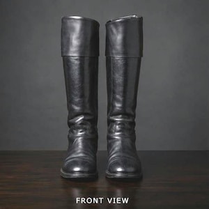 Puede incluir: Un par de botas altas de cuero negro con acabado liso, punta redondeada y una solapa ancha en la parte superior. Las botas tienen una caña estructurada y un aspecto limpio y pulido. El texto FRONT VIEW está impreso en la parte inferior central.