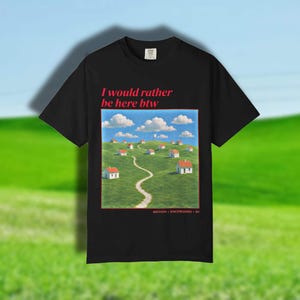 May include: A black t-shirt featuring the red text I would rather be here btw above a graphic of a green grassy hill with small houses and a winding path under a blue sky with white clouds. The text MOTION BACKROOMS 84 is printed in red below.