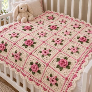 May include: A cream-colored crochet blanket featuring a grid of square panels, each decorated with a three-dimensional pink rose and green leaves. The blanket is bordered by a scalloped edge in pink and cream, with a plush beige toy rabbit nearby.
