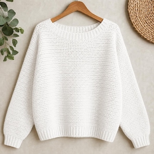 May include: A solid white long-sleeve sweater featuring a textured knit pattern, a wide rounded neckline, and ribbed detailing along the collar, cuffs, and hem. The garment is displayed on a wooden hanger, showcasing a clean and simple design.