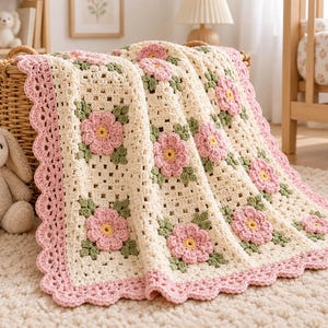 May include: A cream-colored crochet blanket featuring a repeating pattern of pink flowers with yellow centers and green leaves. The blanket has a scalloped pink border and is draped over a woven basket, showcasing intricate yarn work and texture.