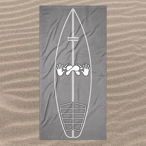 May include: A rectangular grey beach towel featuring a large white line art graphic of a surfboard. The surfboard design includes a central vertical line, a small crown icon, a pair of hands, a pair of feet, and a segmented traction pad at the base.