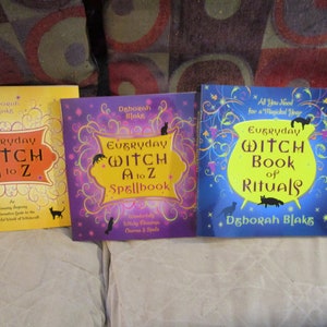 May include: Three books with yellow, purple, and blue covers. The books are titled "Everyday Witch A to Z", "Everyday Witch A to Z Spellbook", and "Everyday Witch Book of Rituals". All three books feature black cats and a whimsical, magical design.
