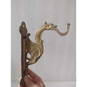 May include: A brass wall hook featuring a stylized dragon design. The hook extends from the dragon's mouth, and the body is intricately detailed. The hook is mounted on a rectangular plate with a decorative top.