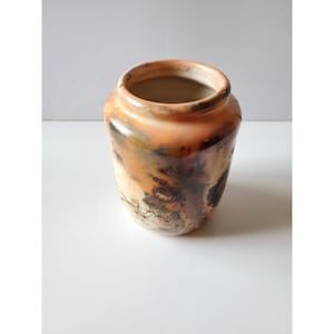 May include: A ceramic vase with a rounded body and a wide opening. The surface features a mottled finish with blended tones of cream, burnt orange, and dark charcoal, creating a smoky, variegated pattern across the exterior of the vessel.