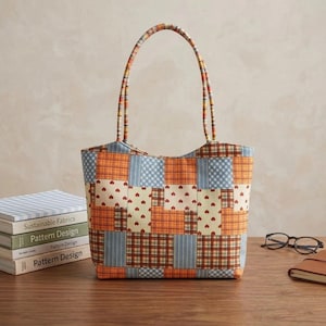 Pode incluir: Uma bolsa tote com design de patchwork composto por quadrados alternados de tecido xadrez laranja, vichy azul claro e tecido creme com pequenos padrões de corações vermelhos. A bolsa tem duas alças de tecido a condizer e uma base retangular.