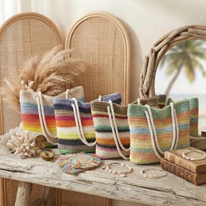Peut inclure: Quatre sacs fourre-tout en crochet avec des anses épaisses en corde blanche, chacun présentant des rayures horizontales dans diverses couleurs pastel et vives. Les sacs sont disposés sur une surface en bois rustique avec des coquillages et des livres.