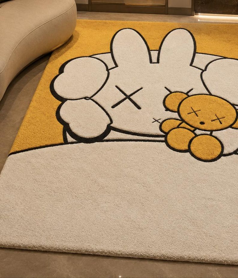 May include: A rectangular rug with a cartoon bunny and teddy bear design. The bunny is white with black outlines and cross-shaped eyes. The teddy bear is yellow with black outlines and cross-shaped eyes. The background is yellow and beige.