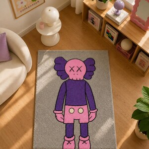 May include: A rectangular gray area rug featuring a central graphic of a cartoon character with a pink skull-shaped head, X-shaped eyes, a purple long-sleeved shirt, pink shorts with two white circular buttons, and pink shoes with cross details.
