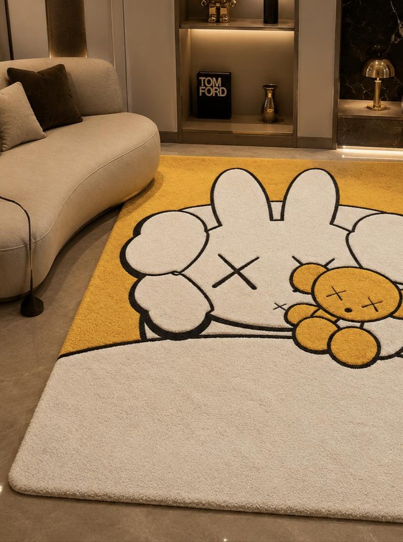 May include: A large, plush area rug featuring a cartoon character design. The rug has a white base with a yellow accent and a large, white character with black outlines and crossed-out eyes. A small, yellow teddy bear is also featured.