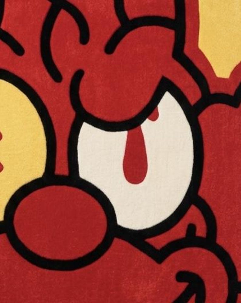 May include: A tufted rug featuring a cartoon-style character face with bold black outlines. The design uses vibrant red, yellow, and white colors, showcasing a large white eye with a red pupil, a red nose, and stylized red facial features.