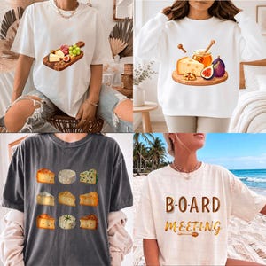 May include: A collection of four shirts and sweatshirts featuring food-themed graphics. Designs include a wooden board with cheese, grapes, and figs, a honey and cheese platter, a grid of various cheese wedges, and the text BOARD MEETING with a honey dipper.