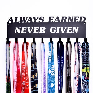 May include: A black metal medal display rack with the words "ALWAYS EARNED NEVER GIVEN" in white lettering. The rack holds 10 medals with colorful ribbons. The medals are from various races and events.