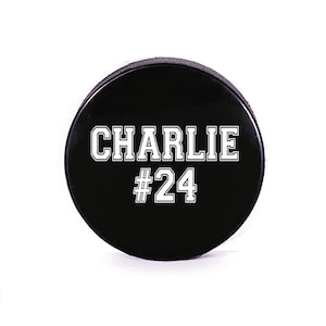 May include: Black hockey puck with white text that reads "CHARLIE #24".
