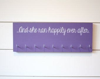 May include: Purple wooden medal hanger with hooks and the text "...And she ran happily ever after."