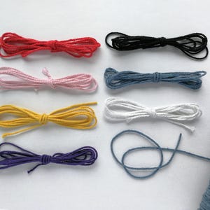 May include: A selection of coloured cords in red, black, pink, blue, yellow, white, purple, and blue. The cords are bundled and tied, with a spool of blue cord visible on the right. Suitable for crafting and DIY projects.