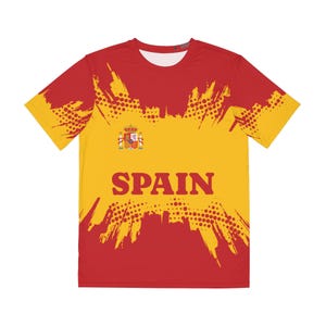 Può includere: Una maglietta a maniche corte con un design giallo e rosso. La maglietta presenta la parola "SPAIN" a lettere grandi, lo stemma spagnolo e un motivo a pois. Il design ricorda la bandiera spagnola.