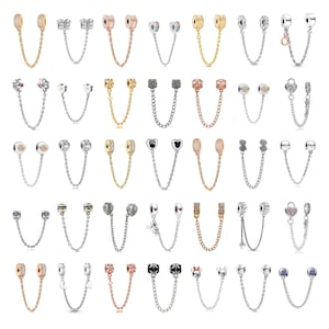 Pode incluir: Uma coleção de trinta correntes de segurança de metal para pulseiras de berloques, com vários designs incluindo corações, estrelas, borboletas e formas geométricas em tons de prata, ouro e ouro rosa, algumas adornadas com pequenos cristais.
